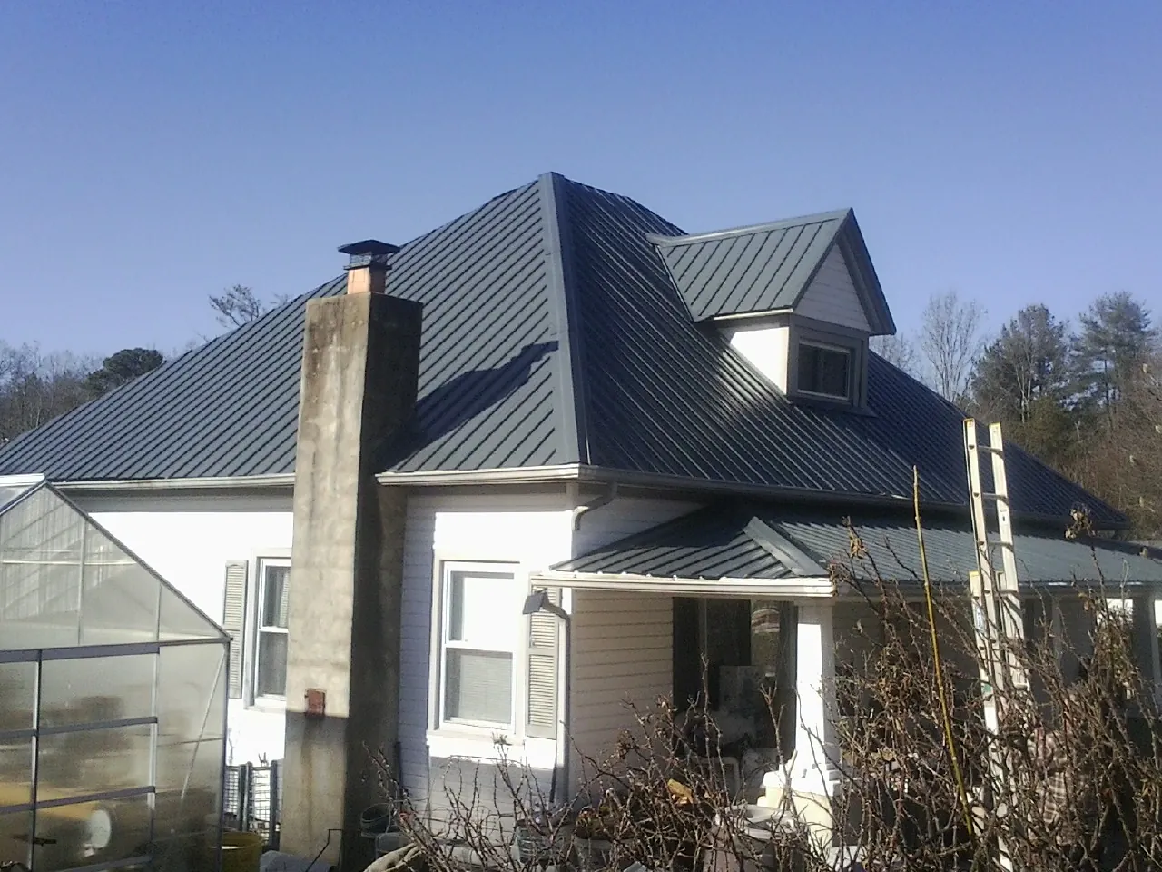 Dark blue standing seam metal roof on a white farmhouse with dormer — Slate & Tile Roof Repair by Roofing Brothers in Helix