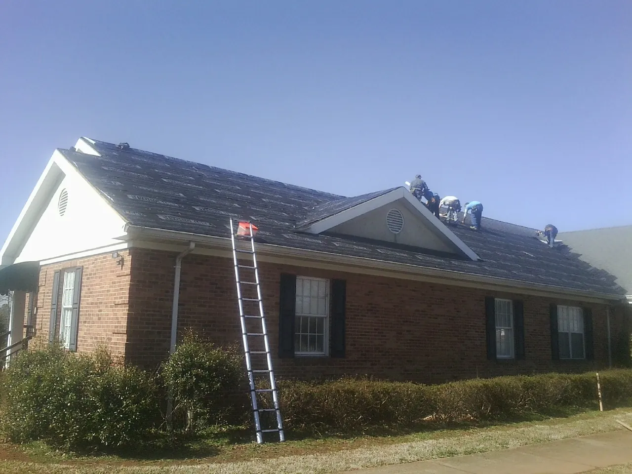 Crew tearing shingles off a brick ranch roof with a ladder set — Emergency Roof Repair work by our crew in Helix