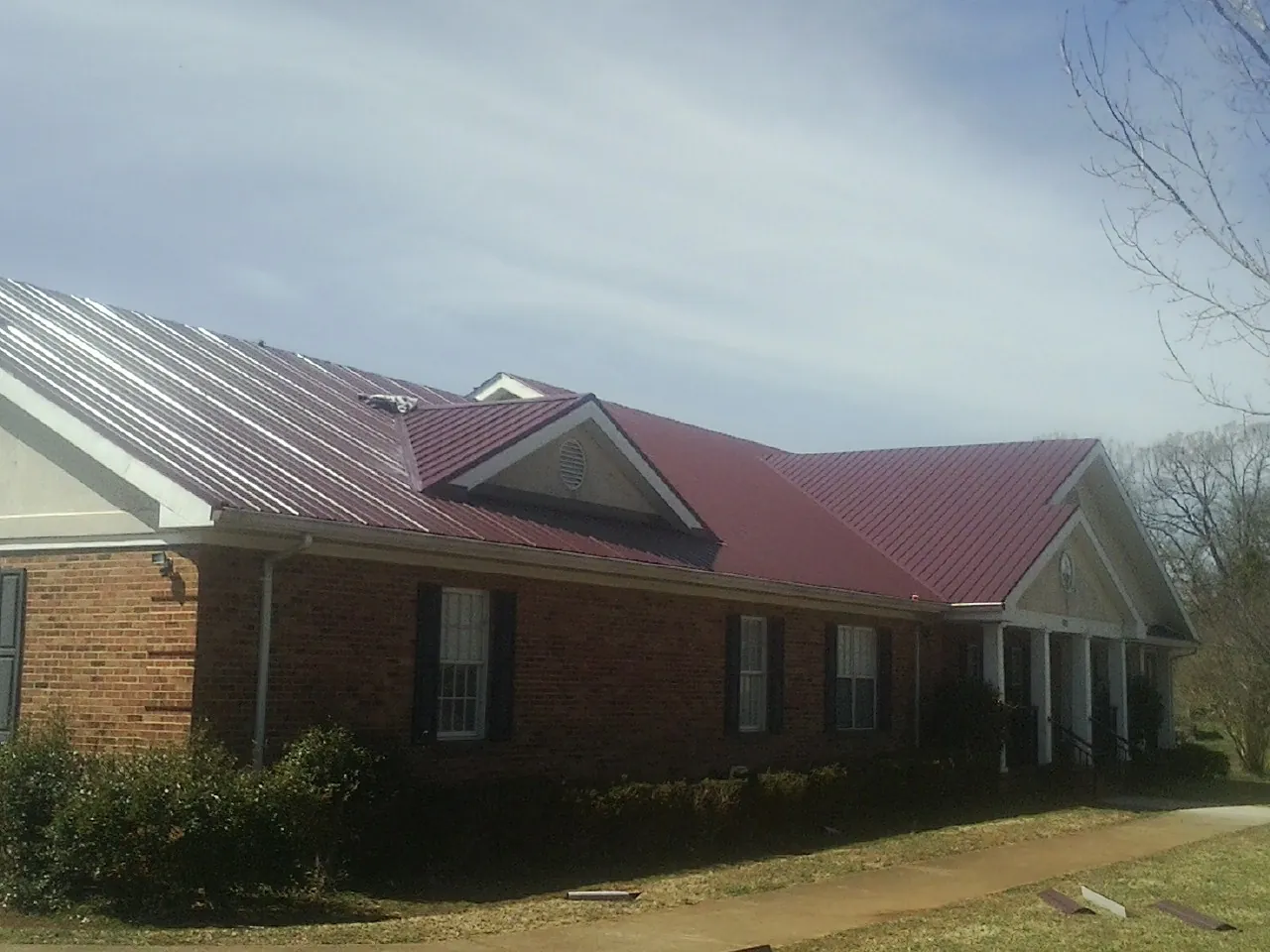 Red metal roof with gabled entries on a long brick building, from a Hail Damage Roof Repair job in Helix
