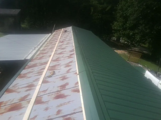 Old rusted panels beside newly installed green metal roofing — Wind Damage Roof Repair by Roofing Brothers in Helix