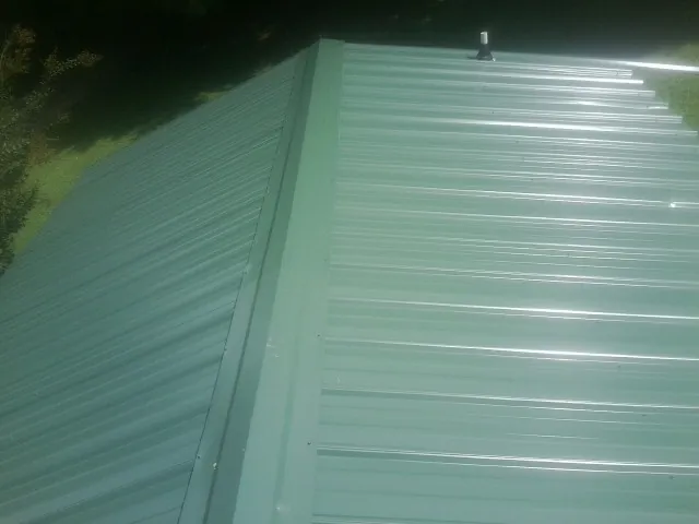 New green metal panels meeting at the ridge of a roof — Flat Roof Repair work by our crew in Helix