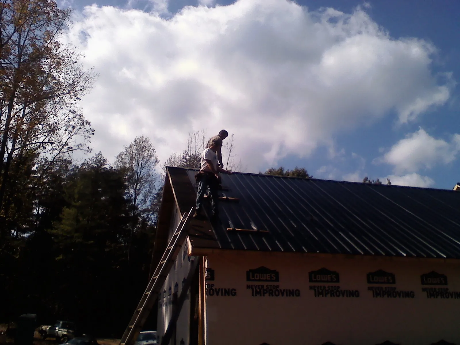 Roofer fastening dark metal panels high against a cloudy sky, from a Roof Inspection job in Helix
