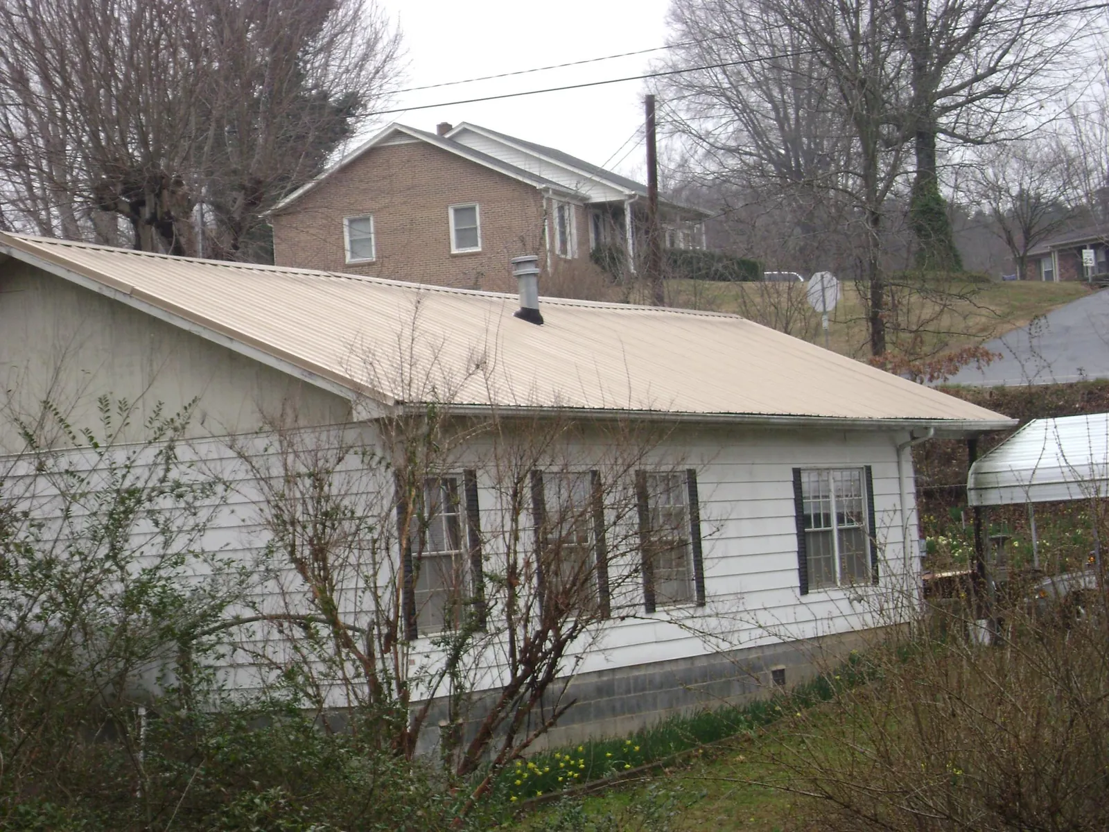 Tan metal roof on a white sided house set into a hillside — Commercial Roofing by Roofing Brothers in Helix